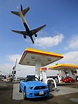 Consumers purchase gasoline at a gas station as a plane approaches to ...