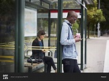 Mid adult commuters waiting at bus stop in city stock photo - OFFSET