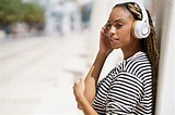 Young black woman listening to music with wireless headphones outdoors ...